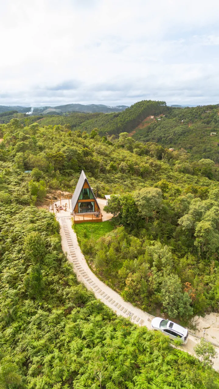Vista aérea do chalé sozinho na mata, com a estrada de chão